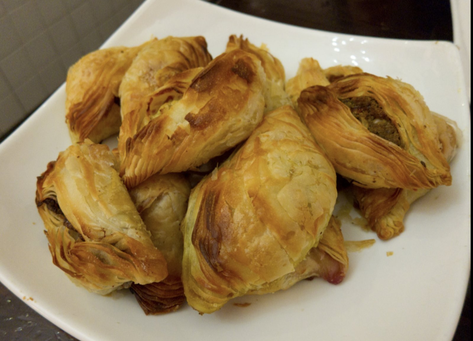Pastizzi recién horneados en un plato blanco, uno de ellos abierto dejando ver el relleno